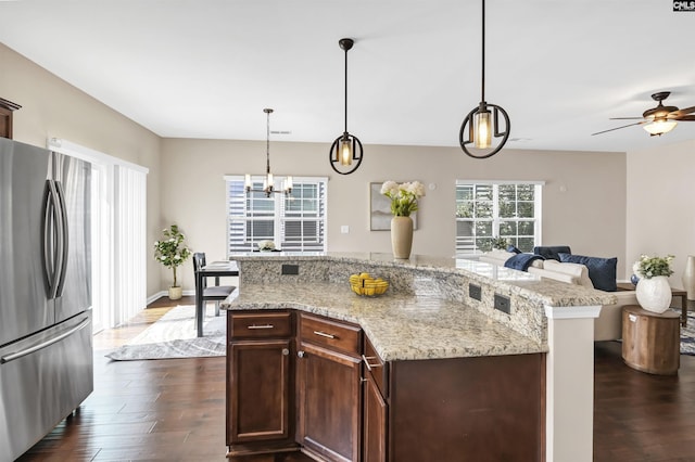 kitchen featuring light stone counters, dark wood-style flooring, freestanding refrigerator, pendant lighting, and open floor plan