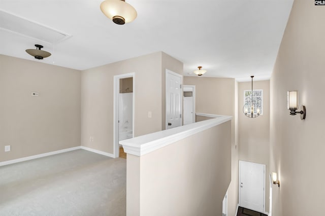 hall featuring a chandelier, baseboards, attic access, and an upstairs landing