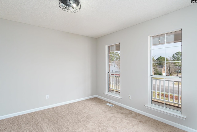 carpeted spare room with visible vents, baseboards, and a textured ceiling