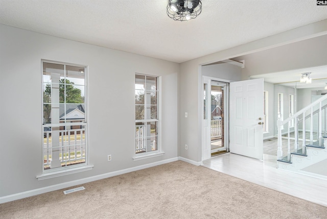 carpeted empty room featuring visible vents, stairway, a textured ceiling, and baseboards