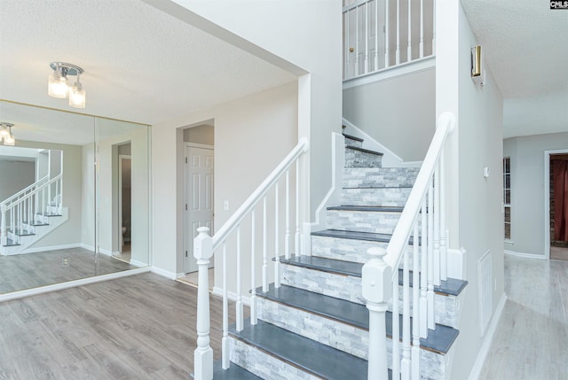 staircase with wood finished floors, baseboards, and a textured ceiling