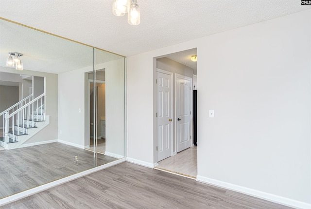 spare room featuring stairway, baseboards, a textured ceiling, and wood finished floors