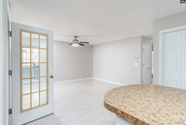 interior space featuring baseboards, a ceiling fan, light wood-style floors, and a textured ceiling