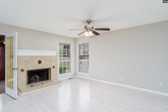 unfurnished living room with visible vents, baseboards, a tile fireplace, wood finished floors, and a ceiling fan