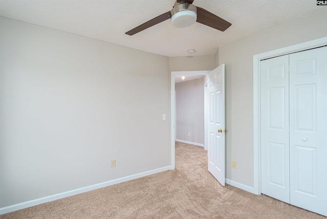 unfurnished bedroom featuring baseboards, ceiling fan, light colored carpet, a closet, and a textured ceiling