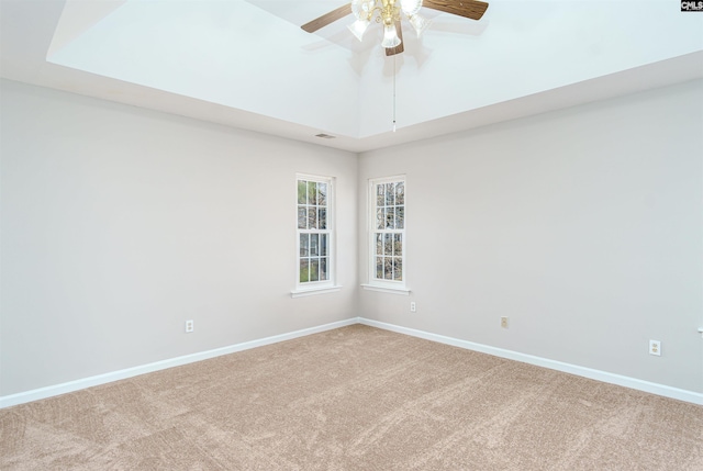 carpeted empty room with vaulted ceiling, baseboards, a tray ceiling, and ceiling fan