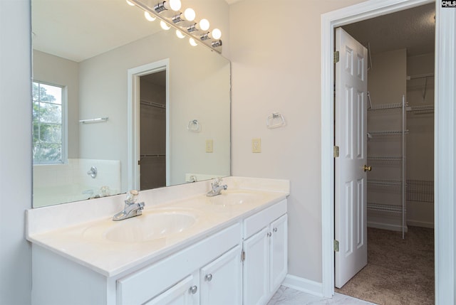 bathroom featuring a sink, baseboards, a spacious closet, and double vanity