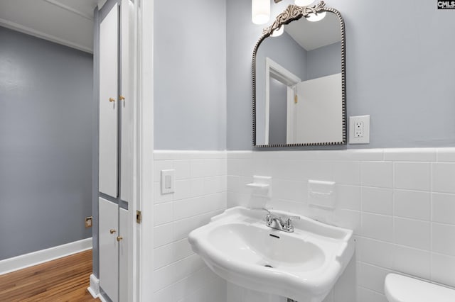 half bath with a wainscoted wall, toilet, a sink, wood finished floors, and tile walls