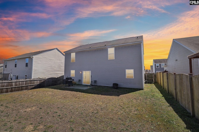 back of house at dusk with a fenced backyard, a lawn, and a patio