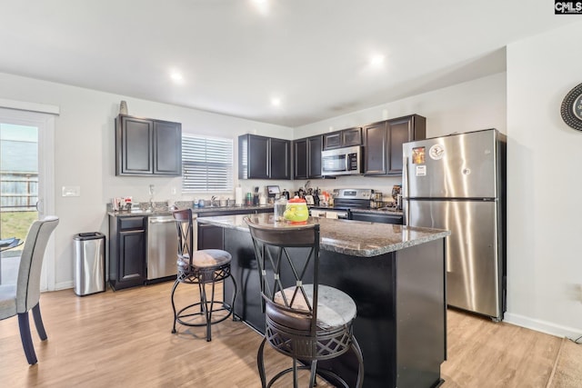 kitchen featuring dark stone countertops, a kitchen island, light wood-style flooring, appliances with stainless steel finishes, and a kitchen breakfast bar