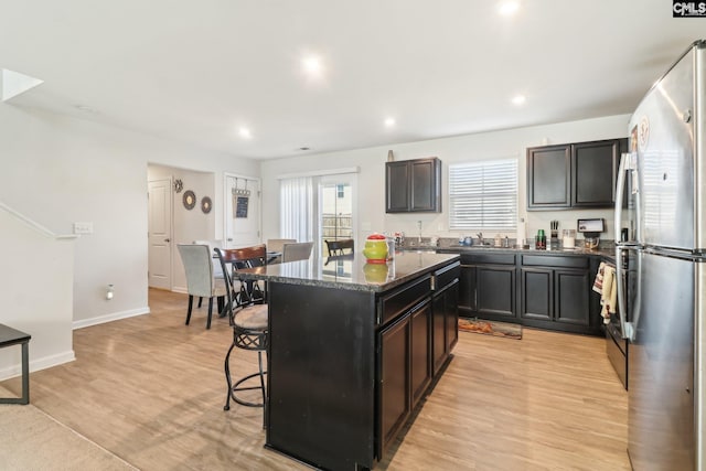 kitchen with a breakfast bar, light wood-style flooring, dark stone countertops, a center island, and freestanding refrigerator