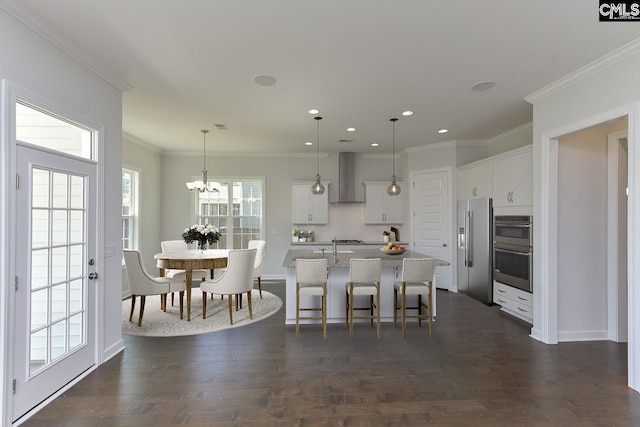 kitchen with a kitchen island with sink, stainless steel appliances, dark wood-type flooring, a kitchen breakfast bar, and wall chimney exhaust hood