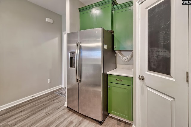 kitchen with baseboards, light wood finished floors, light countertops, green cabinets, and stainless steel fridge