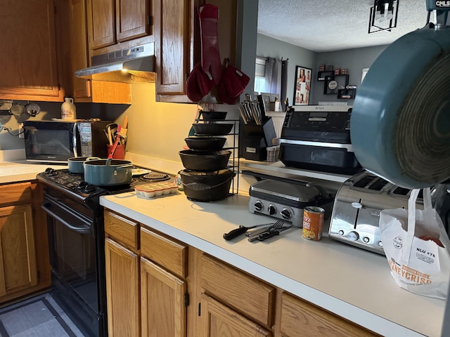 kitchen featuring under cabinet range hood, a textured ceiling, black appliances, and light countertops