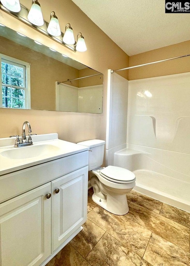 bathroom with vanity, toilet, a shower, and a textured ceiling