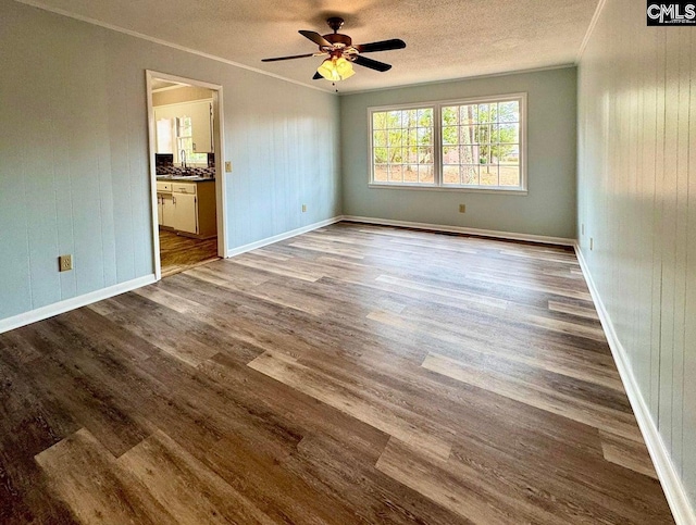 unfurnished room with a ceiling fan, baseboards, dark wood-style flooring, ornamental molding, and a textured ceiling