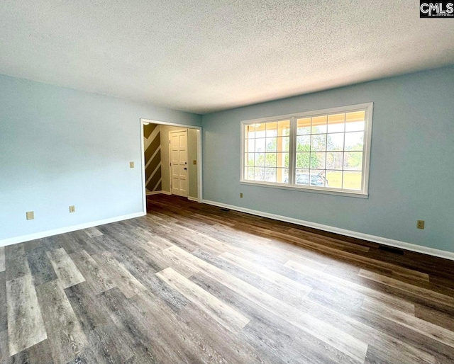 empty room featuring a textured ceiling, baseboards, and wood finished floors