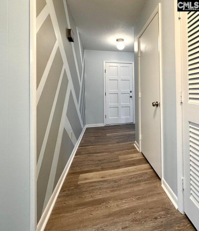 hallway featuring a textured ceiling, baseboards, and wood finished floors