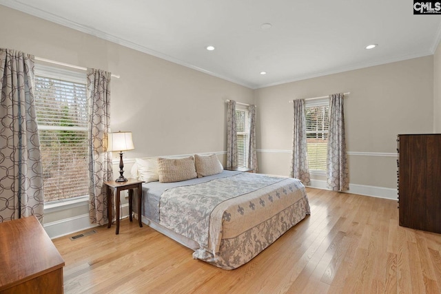 bedroom with visible vents, baseboards, light wood-style floors, and ornamental molding