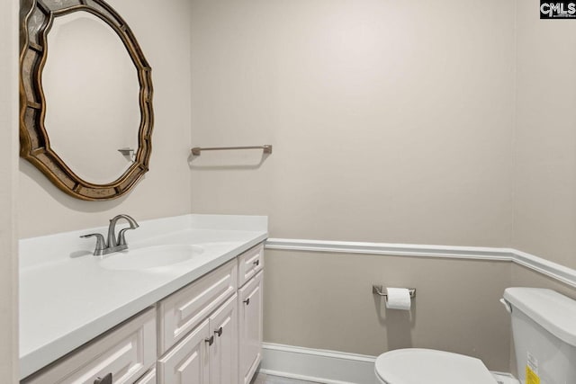 half bathroom featuring baseboards, toilet, and vanity