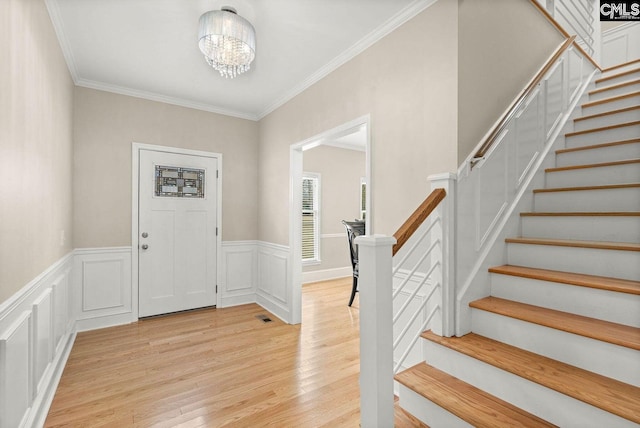 foyer entrance with stairway, a wainscoted wall, ornamental molding, light wood-style floors, and a notable chandelier