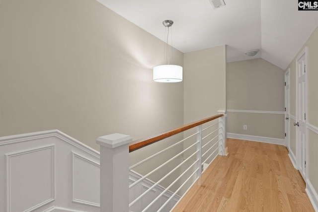 corridor featuring visible vents, an upstairs landing, a wainscoted wall, light wood finished floors, and lofted ceiling