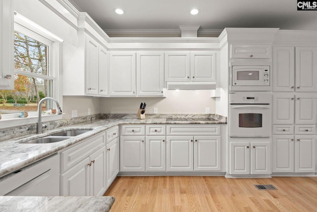 kitchen with under cabinet range hood, ornamental molding, white cabinets, white appliances, and a sink