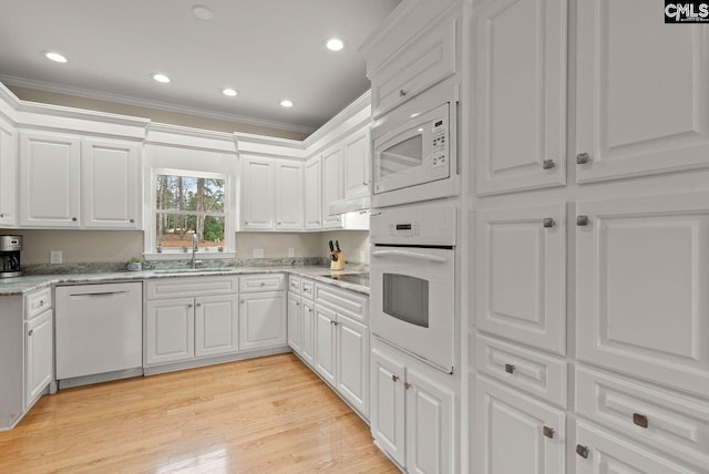 kitchen with light wood finished floors, ornamental molding, white cabinets, white appliances, and a sink