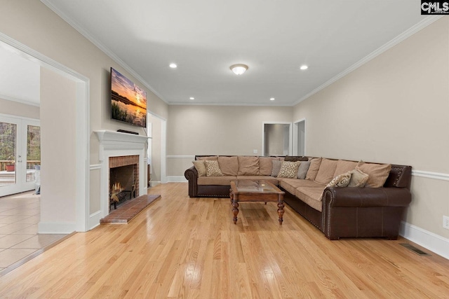 living area with visible vents, light wood-style floors, a brick fireplace, and crown molding