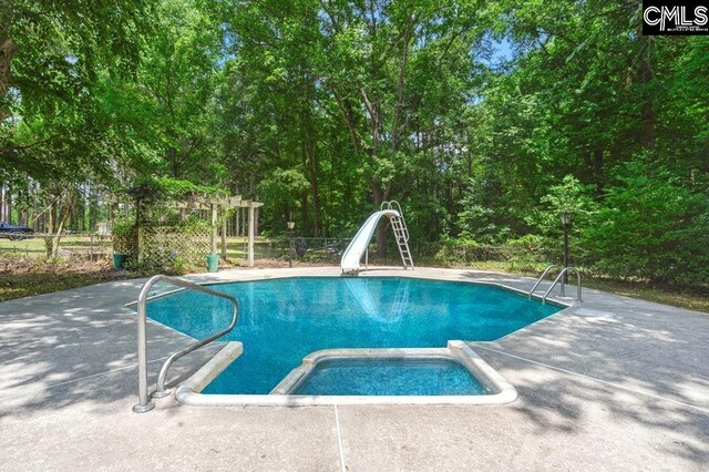 view of pool with a patio area, a pool with connected hot tub, a water slide, and fence