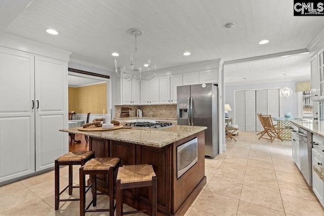 kitchen featuring decorative backsplash, appliances with stainless steel finishes, white cabinets, and an inviting chandelier