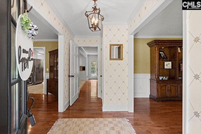 foyer featuring a textured ceiling, ornamental molding, wainscoting, and wallpapered walls