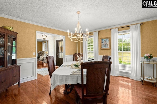 dining room featuring a notable chandelier, hardwood / wood-style flooring, wainscoting, and a textured ceiling