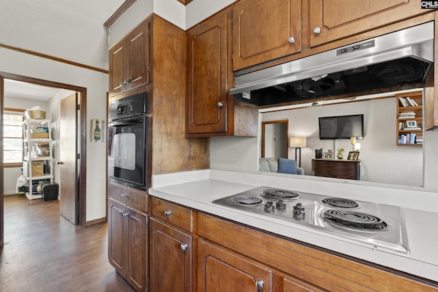 kitchen with black oven, under cabinet range hood, light countertops, ornamental molding, and stainless steel electric stovetop