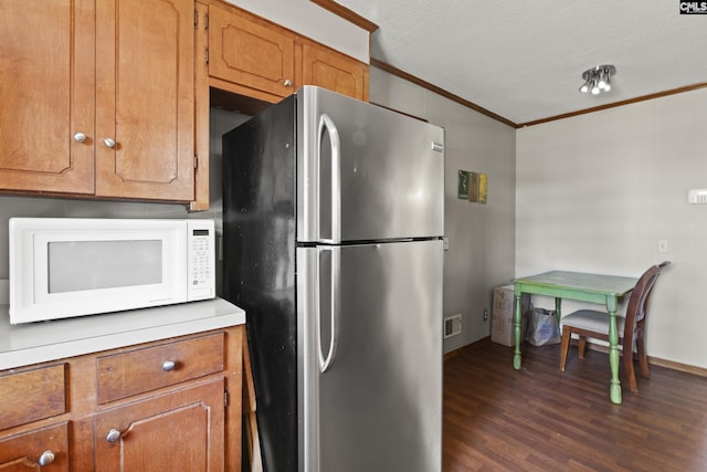 kitchen with white microwave, dark wood finished floors, freestanding refrigerator, ornamental molding, and brown cabinets
