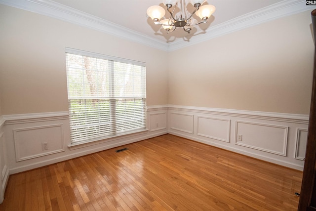 empty room with visible vents, an inviting chandelier, ornamental molding, light wood-style floors, and wainscoting