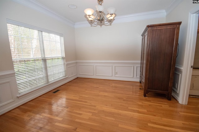 spare room featuring visible vents, an inviting chandelier, light wood-style flooring, and ornamental molding