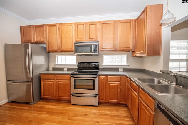 kitchen with dark countertops, a sink, appliances with stainless steel finishes, crown molding, and light wood-type flooring