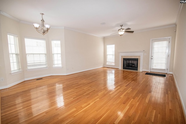 unfurnished living room with ceiling fan with notable chandelier, ornamental molding, a fireplace with flush hearth, and light wood finished floors