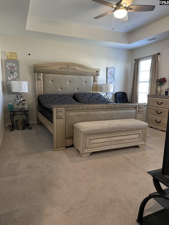 bedroom with visible vents, light colored carpet, a raised ceiling, and ceiling fan
