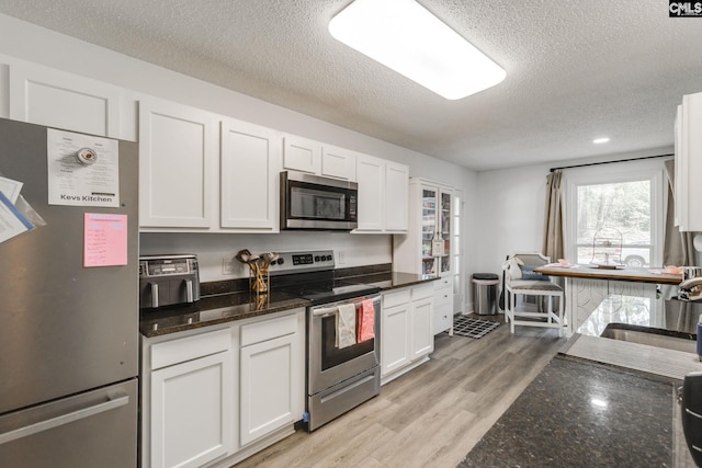 kitchen with light wood finished floors, dark stone countertops, appliances with stainless steel finishes, white cabinets, and a textured ceiling