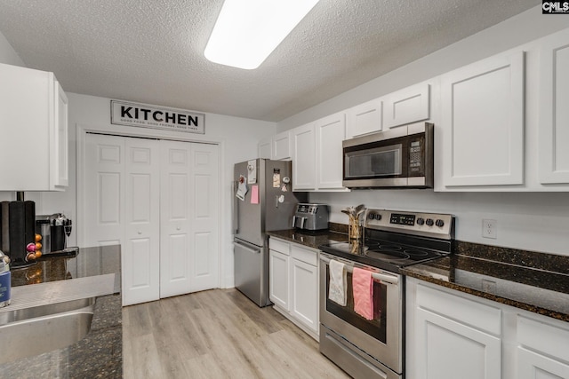 kitchen featuring a textured ceiling, stainless steel appliances, light wood-style floors, and white cabinetry