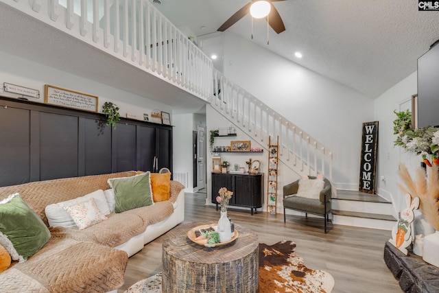 living room featuring stairway, a ceiling fan, wood finished floors, high vaulted ceiling, and a textured ceiling