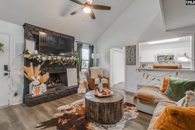 living area with ceiling fan, a fireplace, wood finished floors, a textured ceiling, and high vaulted ceiling