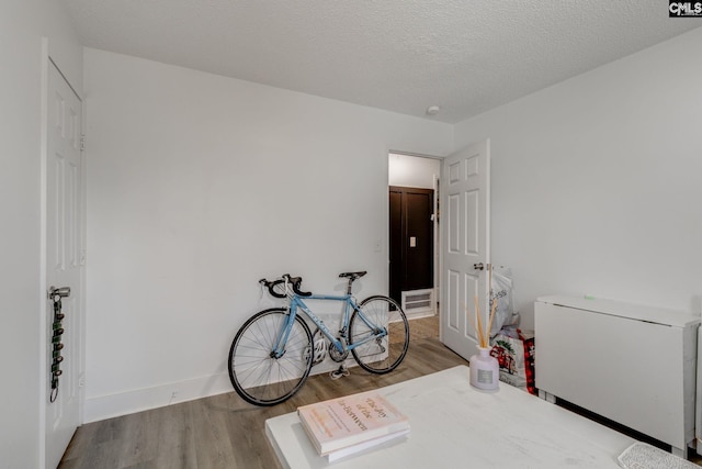 bedroom featuring fridge, wood finished floors, baseboards, and a textured ceiling