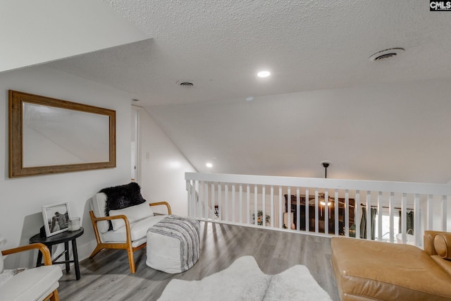 living area with lofted ceiling, wood finished floors, visible vents, and a textured ceiling