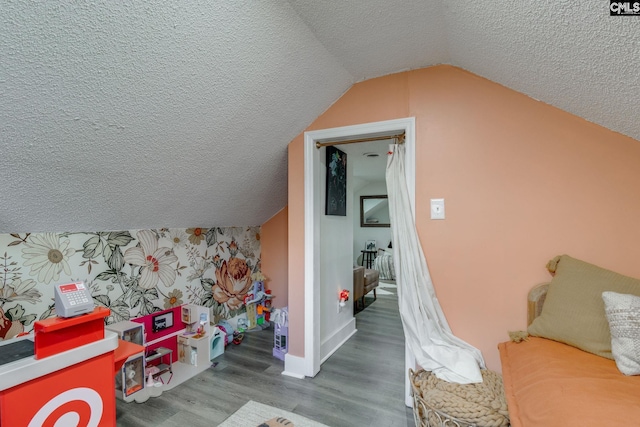 interior space featuring lofted ceiling, a textured ceiling, wood finished floors, wallpapered walls, and baseboards