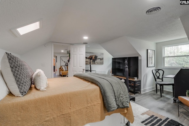 bedroom featuring visible vents, baseboards, lofted ceiling with skylight, wood finished floors, and a textured ceiling