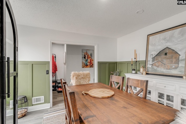 dining area with wood finished floors, a wainscoted wall, visible vents, a textured ceiling, and a decorative wall