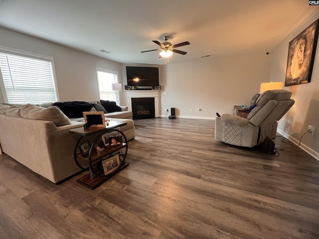 living room with visible vents, baseboards, a fireplace, dark wood-style floors, and a ceiling fan